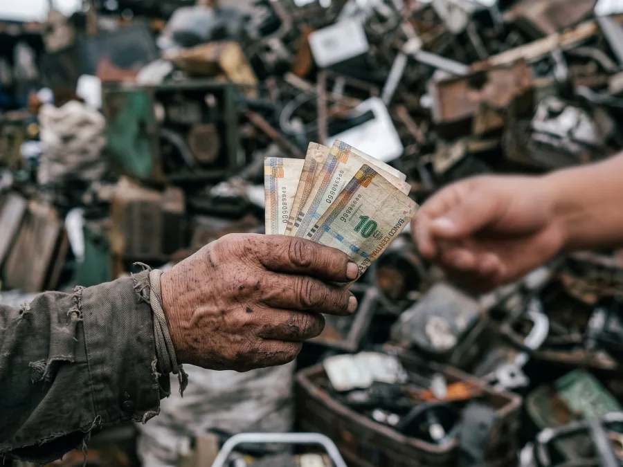 Manos de un reciclador recibiendo unos pocos billetes en un depósito de chatarra